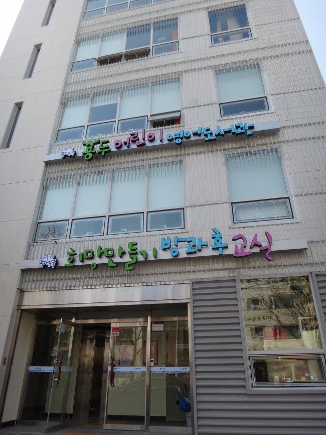 어린이 도서관 건물을 아래에서 올려다본 모습이에요. 벽에 알록달록한 글자가 붙어 있어요.